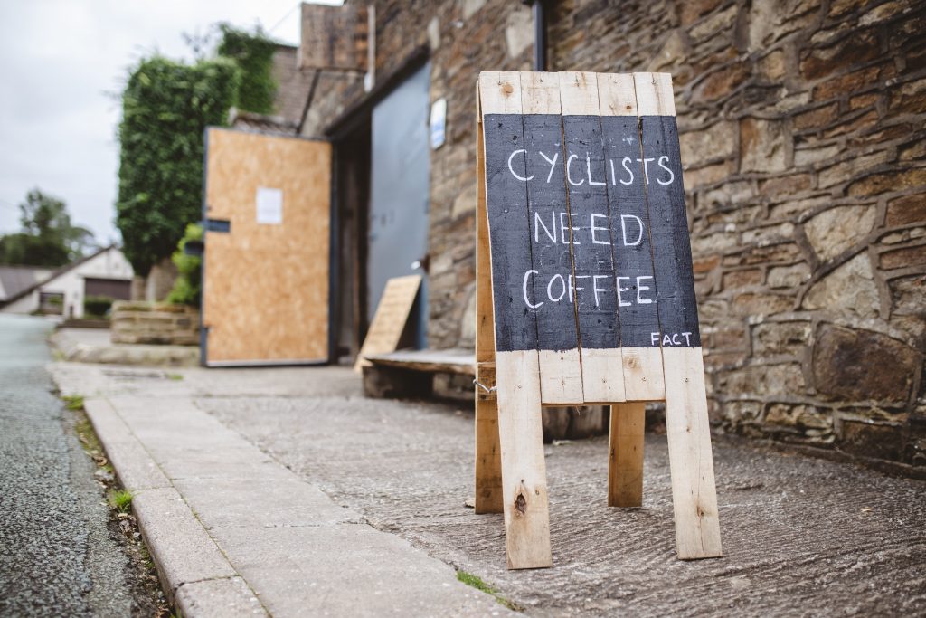 Cyclists need coffee written on wodden a-frame on street pavement.
